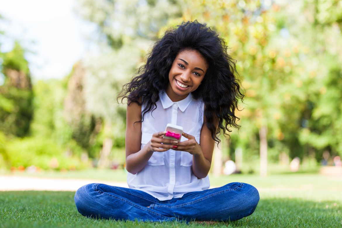 A student sitting on the grass, using a smartphone